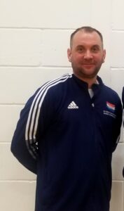 Man in a tracksuit top, with hands behind back